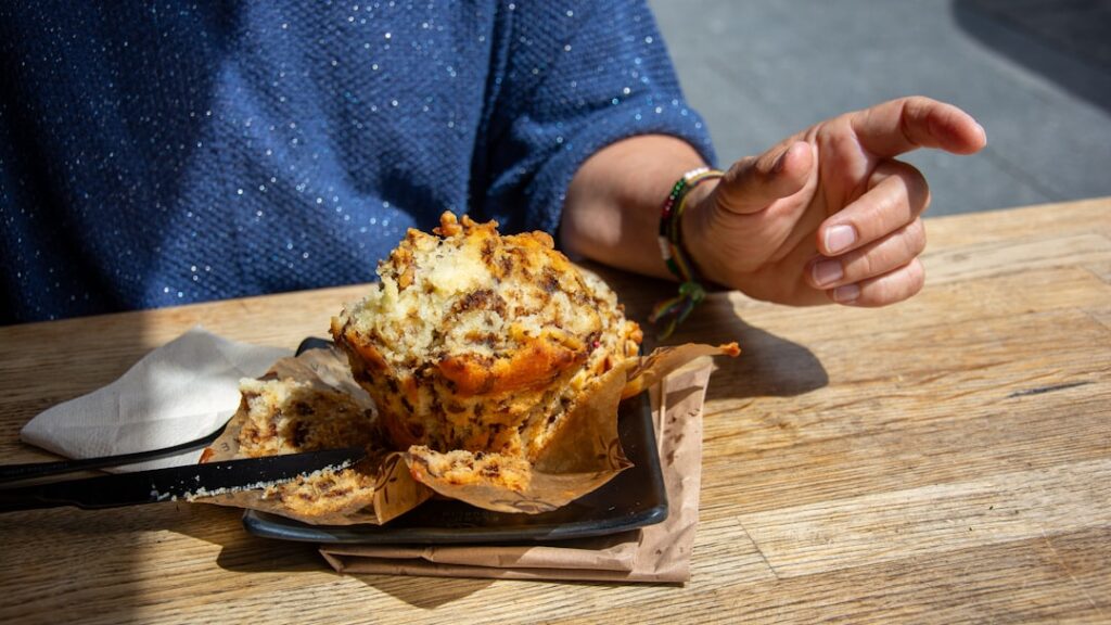 A person eats a muffin at a wooden table