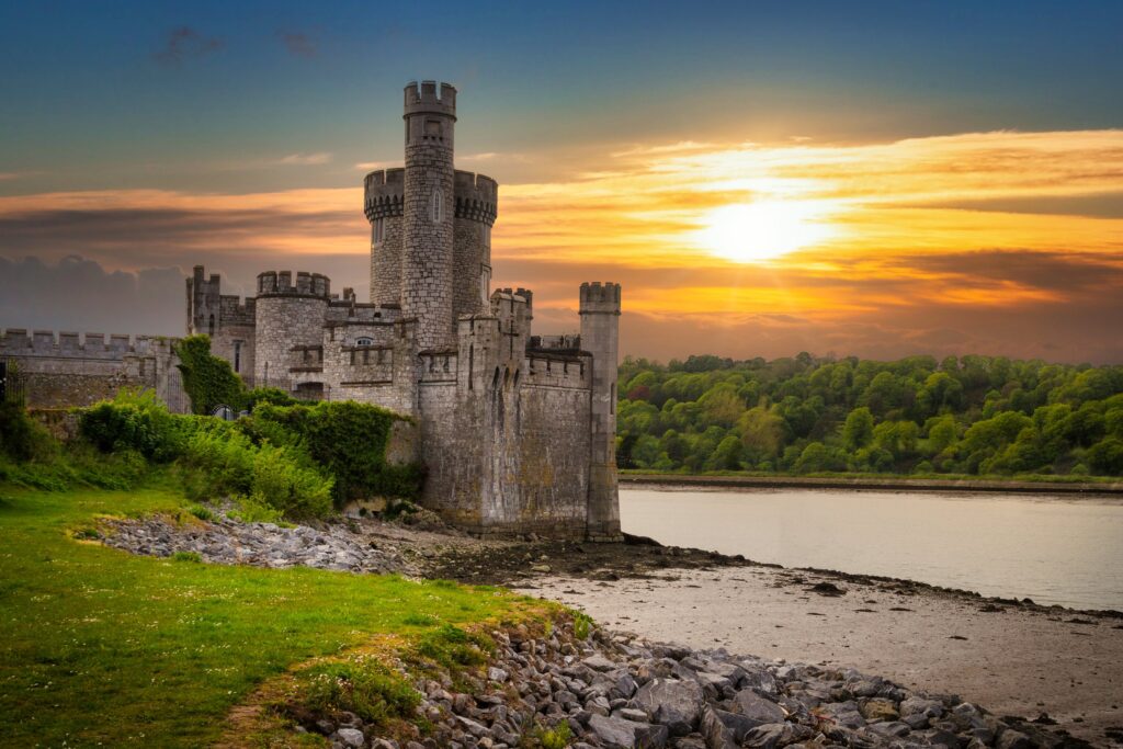 Blackrock Castle on the bank of the River Lee at Cork, Ireland, photographed into a low sun. The castellated grey limestone building stands on a rocky promontory at the left of the frame: a tall round tower with a crenellated and machicolat