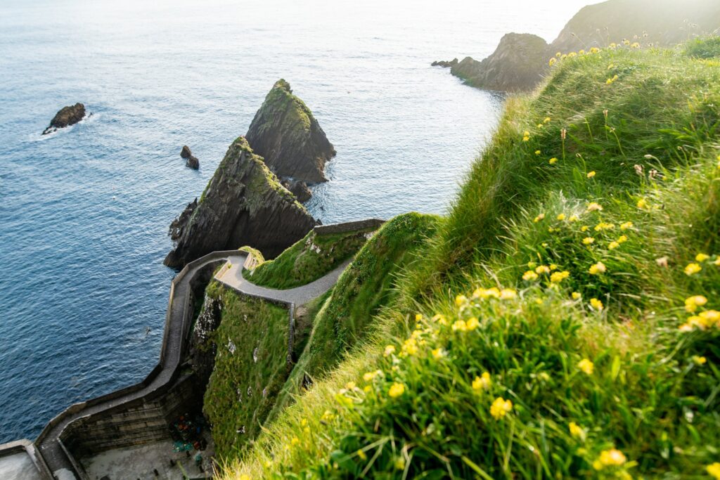 The path down to Dunquin Pier (Dun Chaoin) on the Dingle Peninsula, County Kerry, Ireland. The narrow concrete roadway switchbacks steeply down the left of the frame in tight hairpins, hugging the face of a grassy headland to reach a small