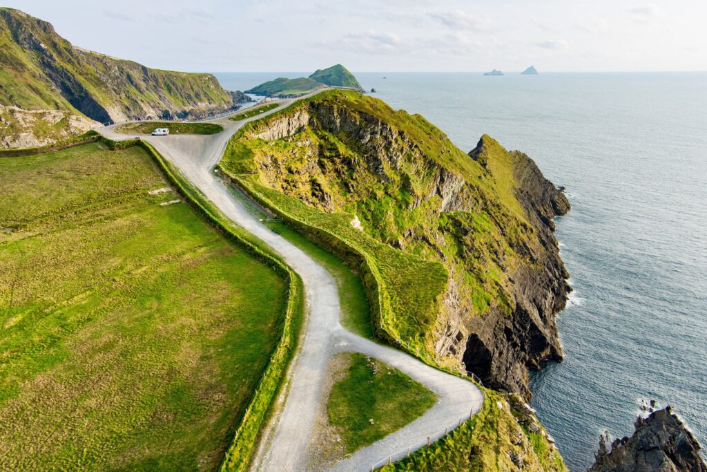 The Kerry Cliffs at Portmagee on the Ring of Kerry, seen from above looking along the clifftop. A narrow gravel visitor path zigzags down the bright green headland in the left and centre of the frame, fenced with low posts, ending at a rail