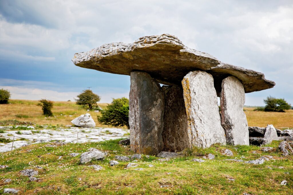 The Poulnabrone portal tomb on the limestone pavement of the Burren, County Clare, Ireland. The dolmen stands slightly left of centre against the sky: a huge thin capstone tilted up towards the left, balanced on two tall upright portal ston