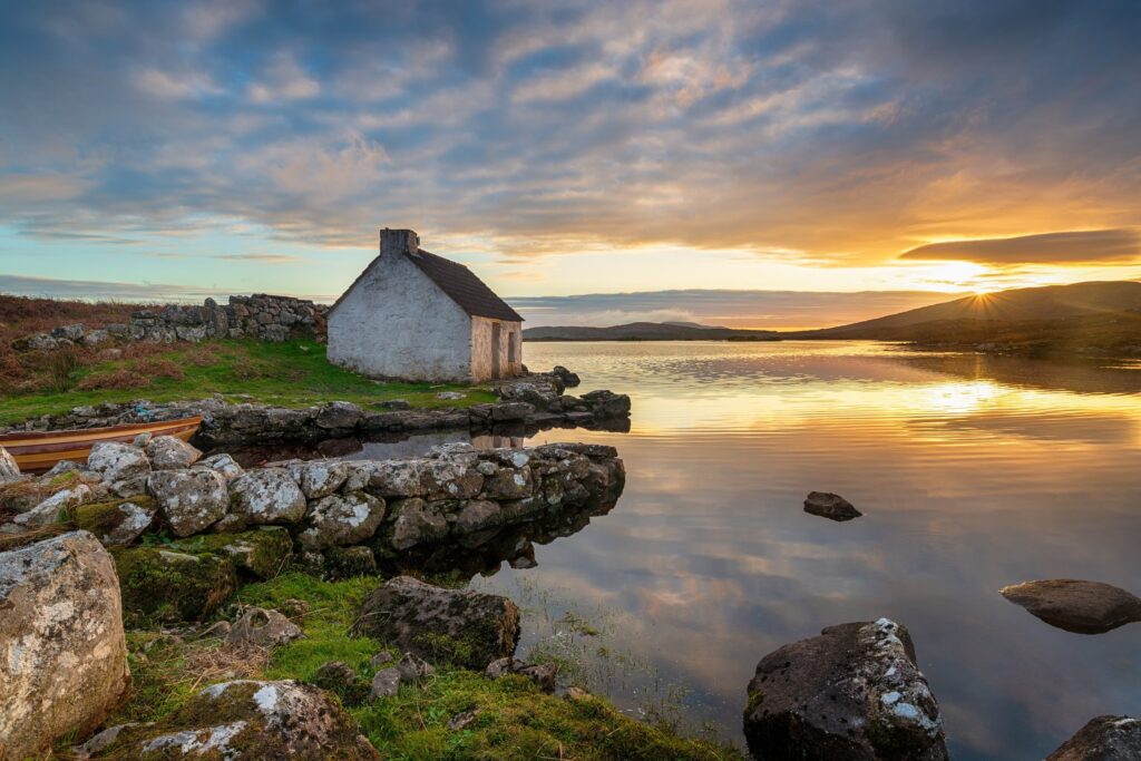 White-washed cottage on rocky shore at golden sunset over water