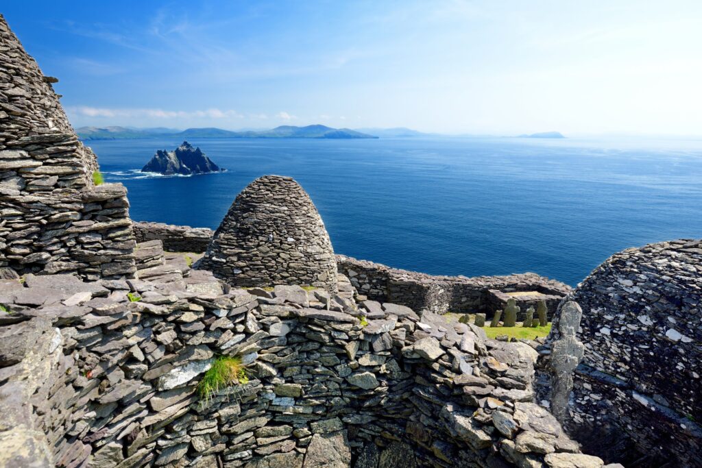 The early medieval monastery on Skellig Michael off the coast of County Kerry, Ireland. Drystone beehive huts with corbelled domed roofs stand among rough stone walls on a terrace high above the sea, their grey slabs laid without mortar, wi